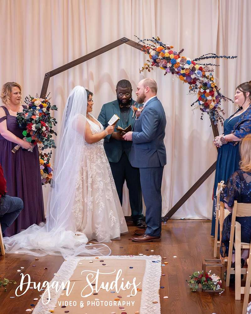 Bride and groom exchanging vows in front of wedding arch
