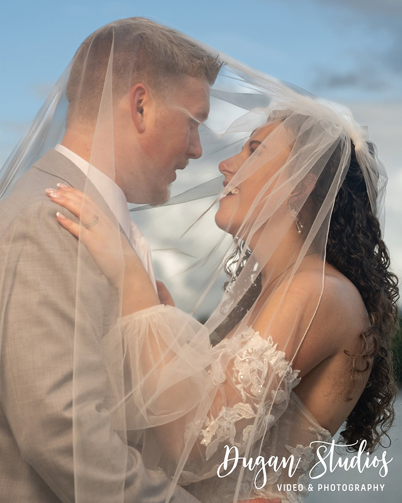 Bride and groom smiling at each other under bride's veil